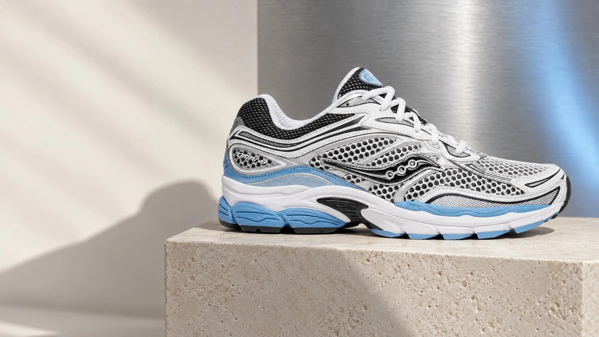 Yenoto AI campaign: a silver and ice-blue Saucony ProGrid Omni 9 trainer on a limestone plinth