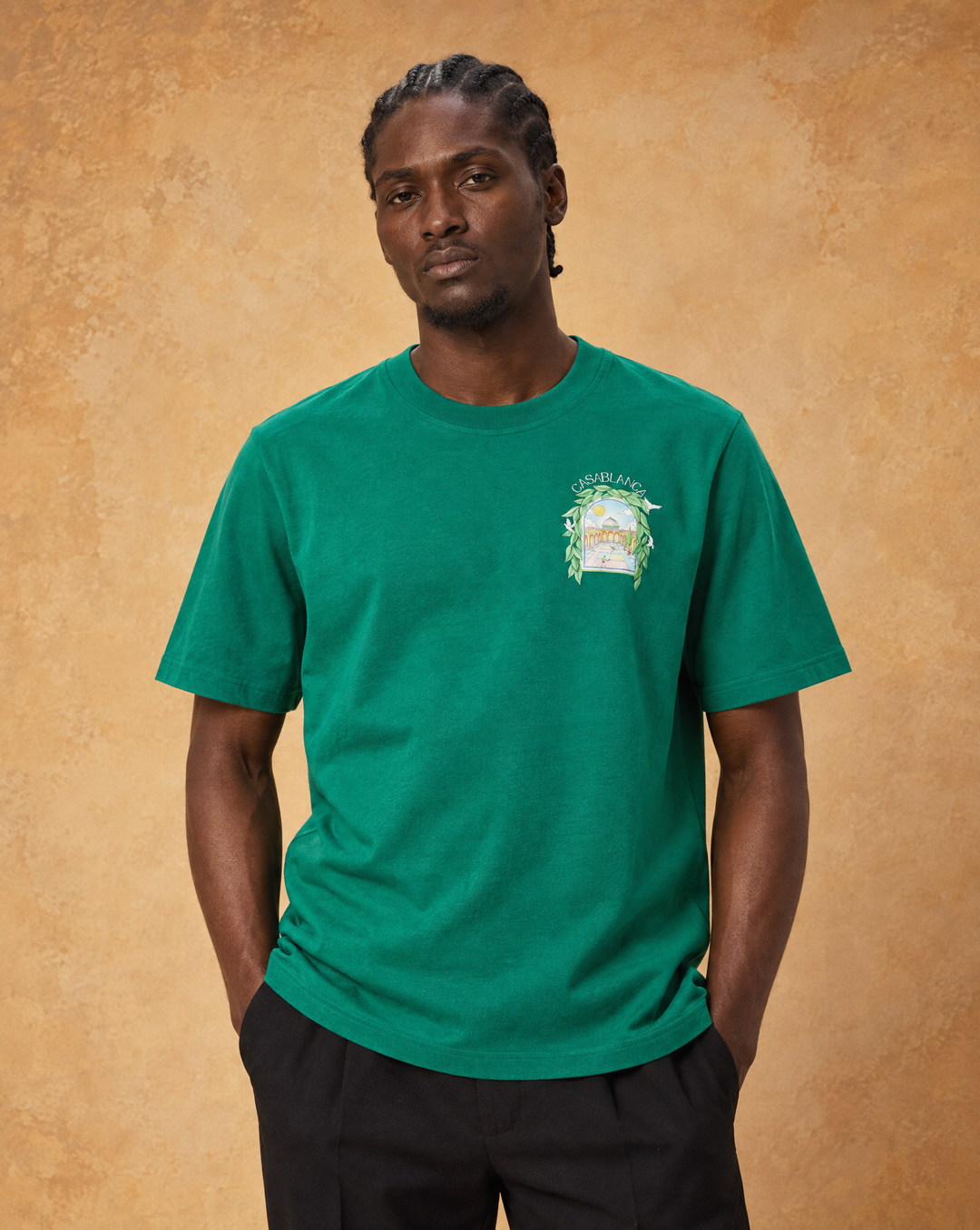 Same male model as the studio preset, waist-up, facing camera, relaxed natural pose, warm ochre studio backdrop, soft daylight, tee worn naturally, no text or props @Casablanca L’Arch De Tennis Tee Green